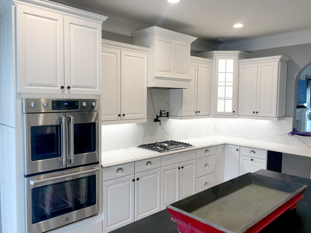 Kitchen with stainless steel appliaces, white granite countertops, and refinished white cabinets with black knobs and drawers with modern silver handles.