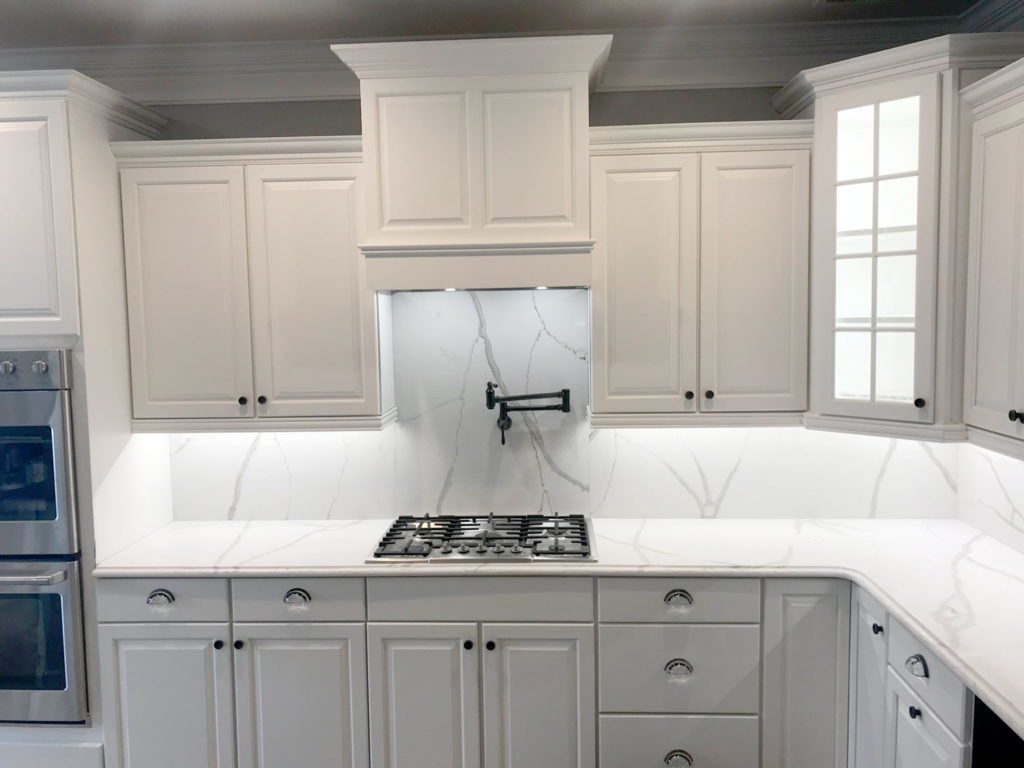 White granite countertop with a black stove kitchenn, stainless steel applicances and white refinished cabintts and drawers by Hartley Group Coatings.