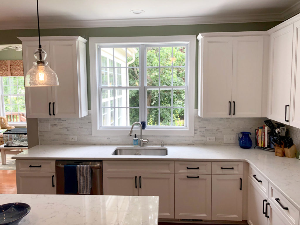 Kitchen sink with window above it, surrounded by Hartley Group Coatings white mitered cabinet doors and drawers with modern black handles.