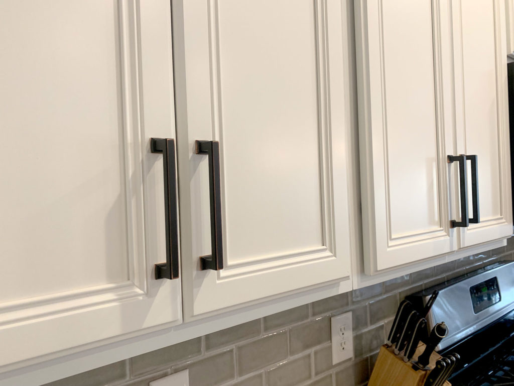 Refinished kitchen cabinets from Hartley Group Coatings. The cabinet doors are painted in white, with modern black handles.