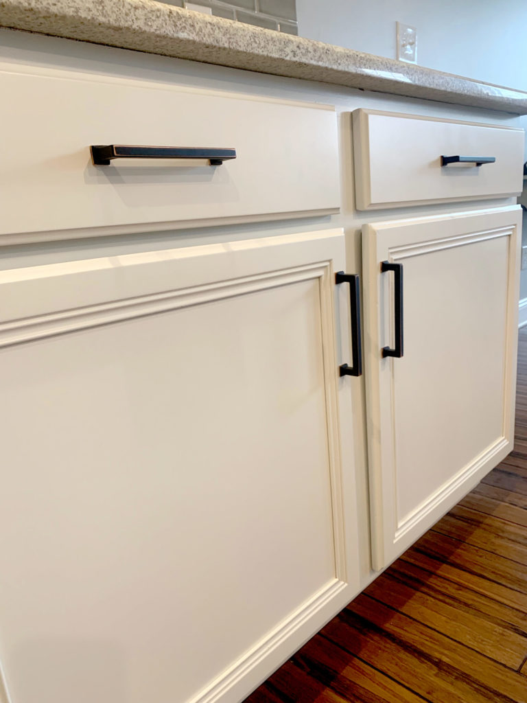 A close-up view of Hartley Group Coatings white refinished mitered cabinets and drawers with black handles, beige countertop, and wooden flooring.